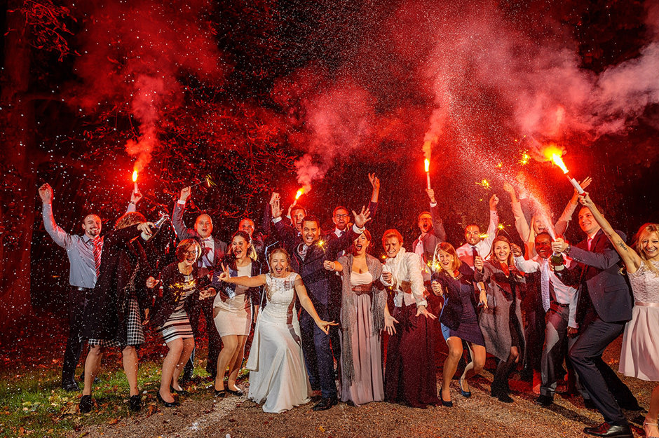Hochzeitsgäste mit spritzendem Sekt und roten Bengalos während der Hochzeitsfeier