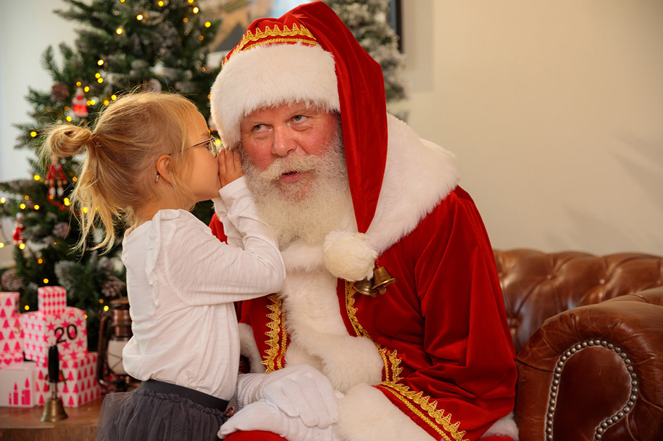 Ein Mädchen flüstert dem Weihnachtsmann beim Fotoshooting in Potsdam ihre Wunschliste ins Ohr.