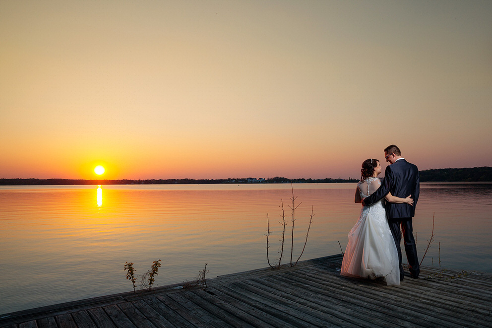 Brautpaar beobachtet den Sonnenuntergang am Wasser