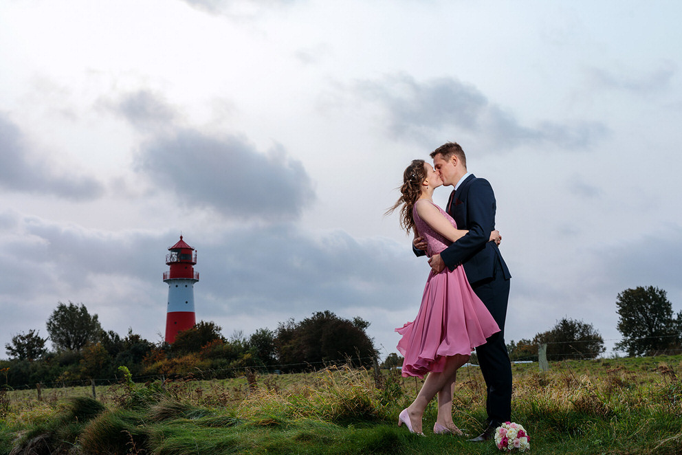 Brautpaar küsst sich vor Leuchtturm am Meer