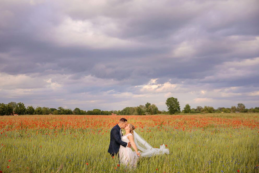 Strahlendes Brautpaar bei Fotos im Mohnblumenfeld bei Sonnenuntergang